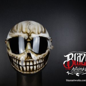 Cracked skull motorcycle helmet design with grinning teeth, bone-colored airbrush art on dark background with reflective visor